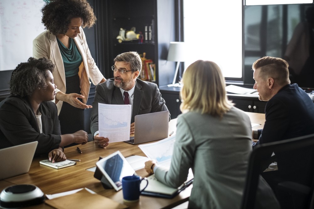 Pessoas ao redor de uma mesa em reunião, momentos em que o inglês profissional pode ser necessário. 