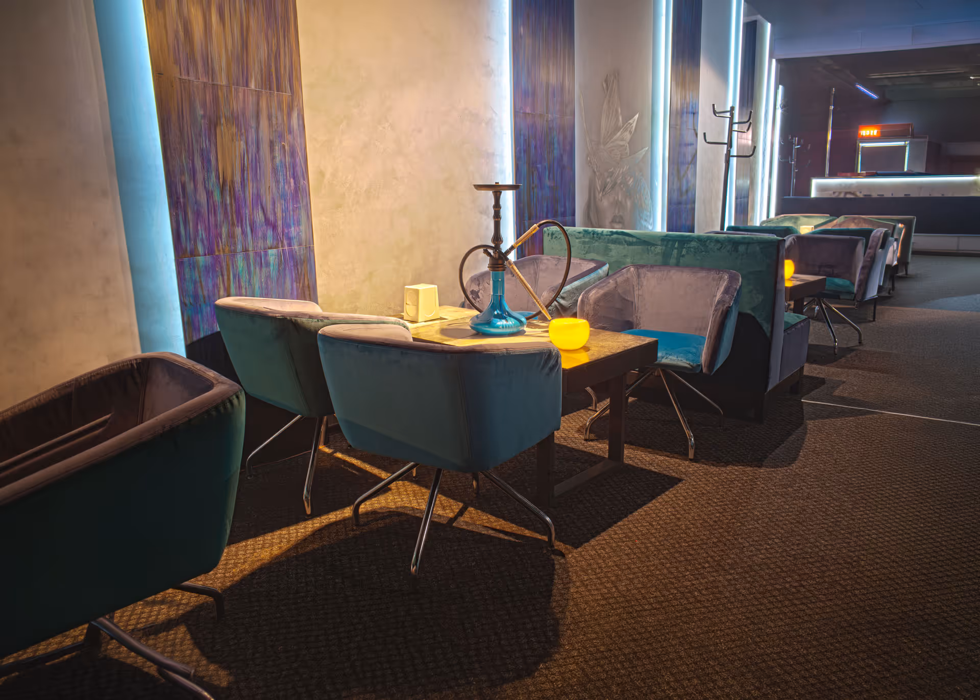 Indoor lounge with velvet chairs around tables, a hookah on one, and soft ambient lighting.