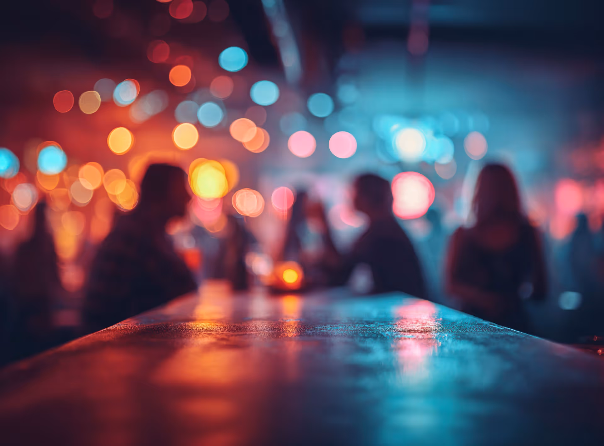 Blurred bar scene with colorful bokeh lights and silhouettes of people socializing.