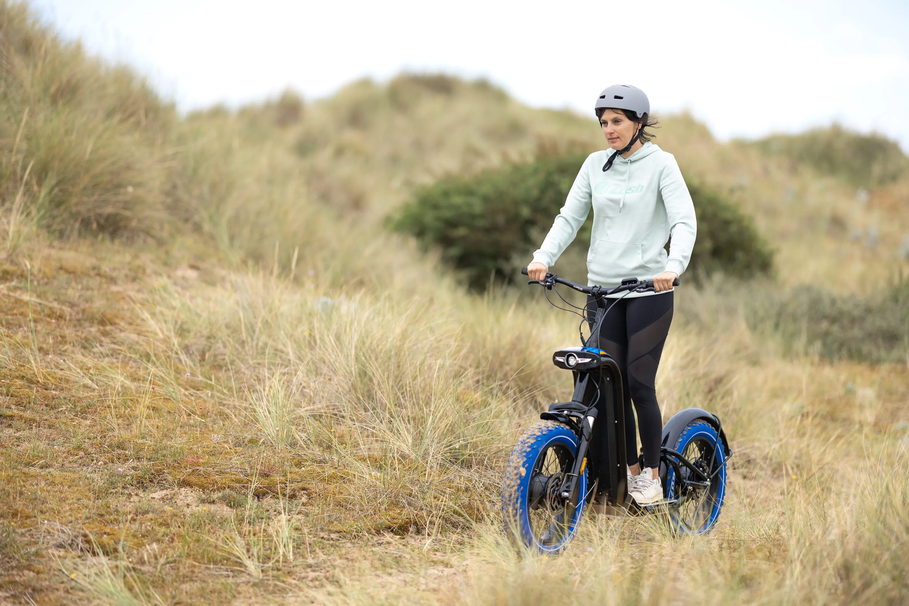 Femme portant un casque en trottinette électrique tout-terrain sur un chemin herbeux.