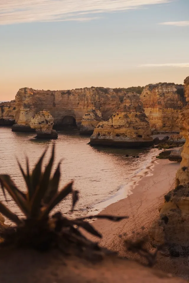 Une plage de sable au coucher du soleil avec des formations rocheuses spectaculaires en bord de mer.