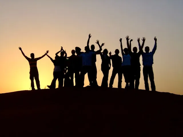 Silhouettes d'un groupe de personnes sur une colline avec les bras levés au coucher du soleil.