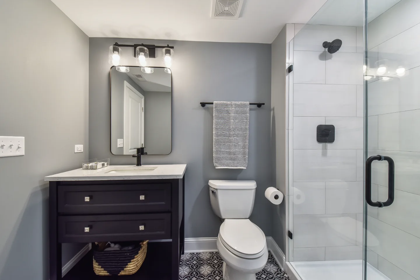 A modern-cool basement guest bath in Brentwood, TN. Jeffery Alexander Alder Black vanity, Corian Coarse Carrara quartz, Kohler Caxton White sink, Kohler Hygiene Classic toilet, and Virginia Tile Deco Anthology 8x8 floor by Sebring Design Build.