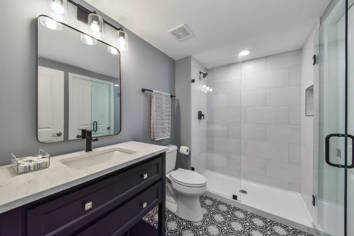 A modern-cool basement guest bath in Brentwood, TN. Jeffery Alexander Alder Black vanity, Corian Coarse Carrara quartz, Kohler Caxton White sink, Kohler Hygiene Classic toilet, and Virginia Tile Deco Anthology 8x8 floor by Sebring Design Build.