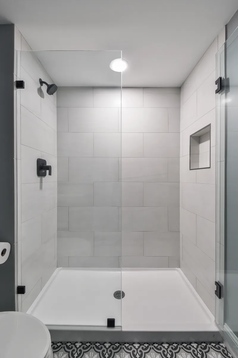 A modern-cool basement guest bath in Brentwood, TN. Jeffery Alexander Alder Black vanity, Corian Coarse Carrara quartz, Kohler Caxton White sink, Kohler Hygiene Classic toilet, and Virginia Tile Deco Anthology 8x8 floor by Sebring Design Build.