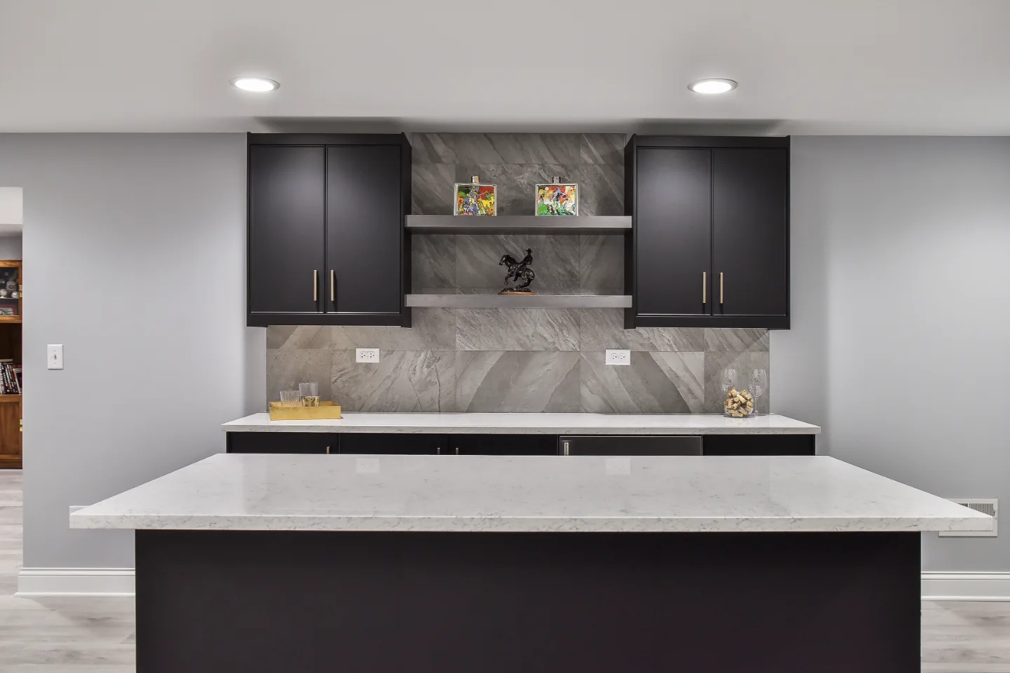 A modern-cool basement bar in Brentwood, TN. Bellmont Apex Matte Black cabinetry, Corian Coarse Carrara quartz, Moen Genta Matte Black faucet, and Galaxy Porcelain Silver/Matte backsplash by Sebring Design Build.