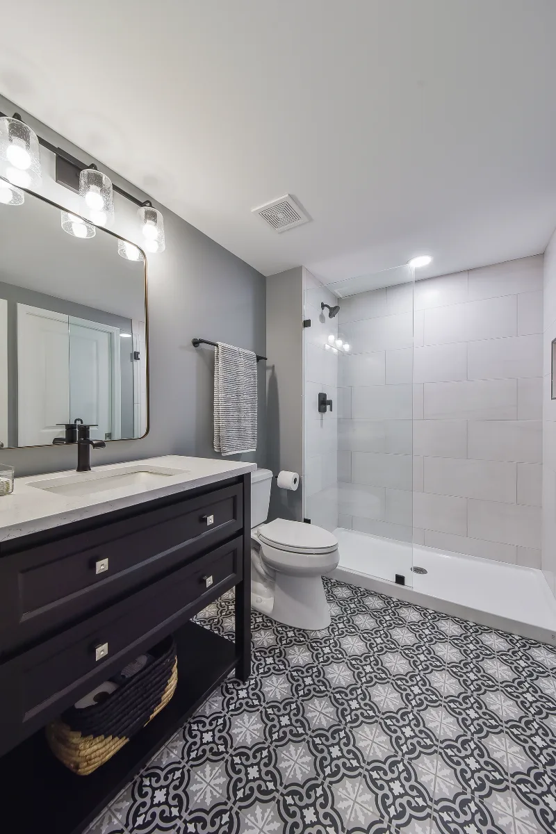 A modern-cool basement guest bath in Brentwood, TN. Jeffery Alexander Alder Black vanity, Corian Coarse Carrara quartz, Kohler Caxton White sink, Kohler Hygiene Classic toilet, and Virginia Tile Deco Anthology 8x8 floor by Sebring Design Build.