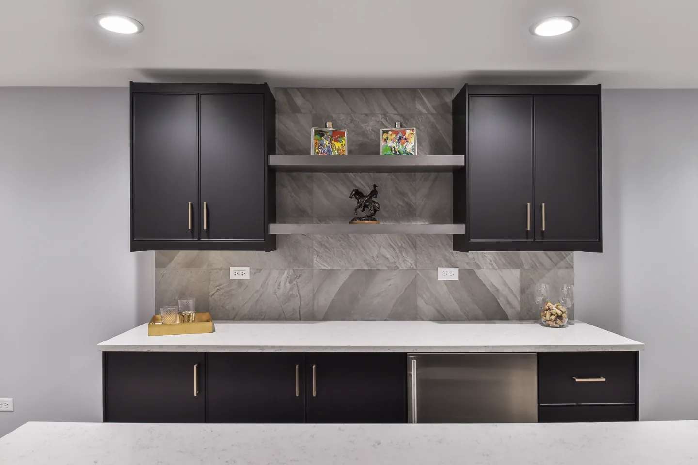 A modern-cool basement bar in Brentwood, TN. Bellmont Apex Matte Black cabinetry, Corian Coarse Carrara quartz, Moen Genta Matte Black faucet, and Galaxy Porcelain Silver/Matte backsplash by Sebring Design Build.