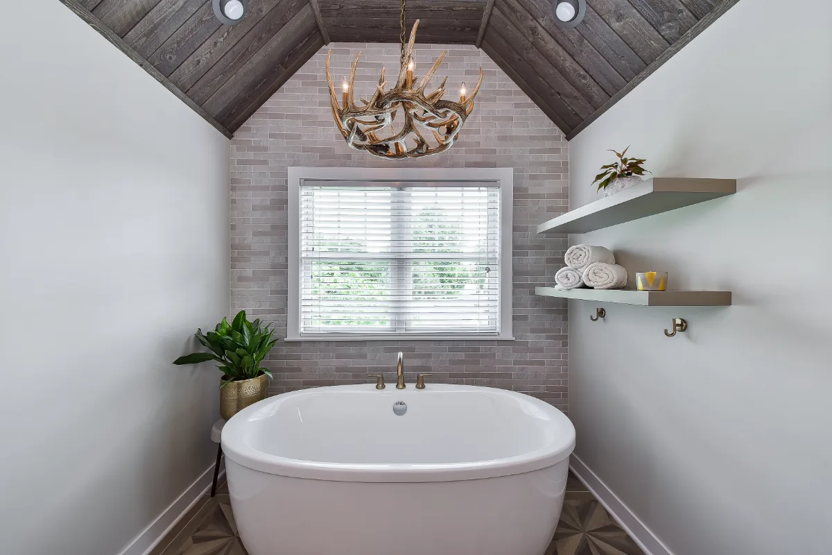 A rustic-warm primary bath in Franklin, TN. Bellmont Alder Folkstone cabinetry with Griege floating shelves, Orion Blanco Mist quartz, Delta Trinsic Champagne Bronze, Kohler Sunstruck tub, and Cassettone Honey Nut wood-look floor tile by Sebring.