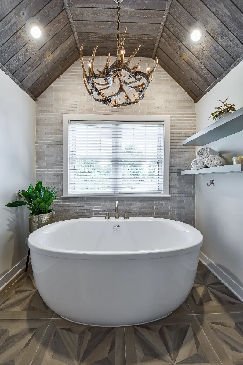 A rustic-warm primary bath in Franklin, TN. Bellmont Alder Folkstone cabinetry with Griege floating shelves, Orion Blanco Mist quartz, Delta Trinsic Champagne Bronze, Kohler Sunstruck tub, and Cassettone Honey Nut wood-look floor tile by Sebring.