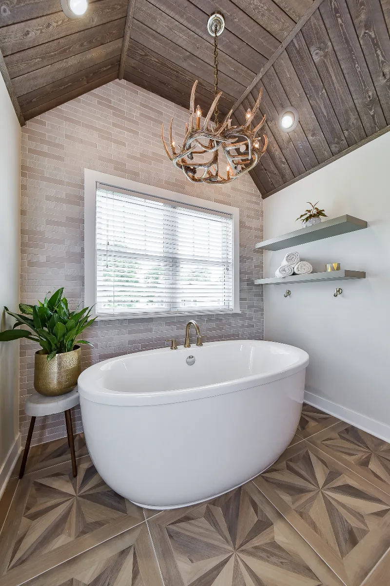 A rustic-warm primary bath in Franklin, TN. Bellmont Alder Folkstone cabinetry with Griege floating shelves, Orion Blanco Mist quartz, Delta Trinsic Champagne Bronze, Kohler Sunstruck tub, and Cassettone Honey Nut wood-look floor tile by Sebring.