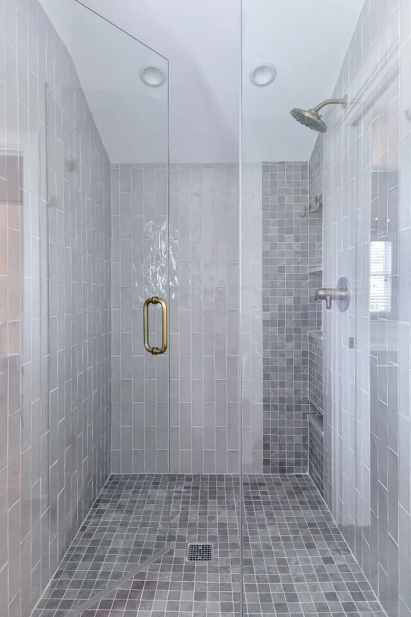 A rustic-warm primary bath in Franklin, TN. Bellmont Alder Folkstone cabinetry with Griege floating shelves, Orion Blanco Mist quartz, Delta Trinsic Champagne Bronze, Kohler Sunstruck tub, and Cassettone Honey Nut wood-look floor tile by Sebring.