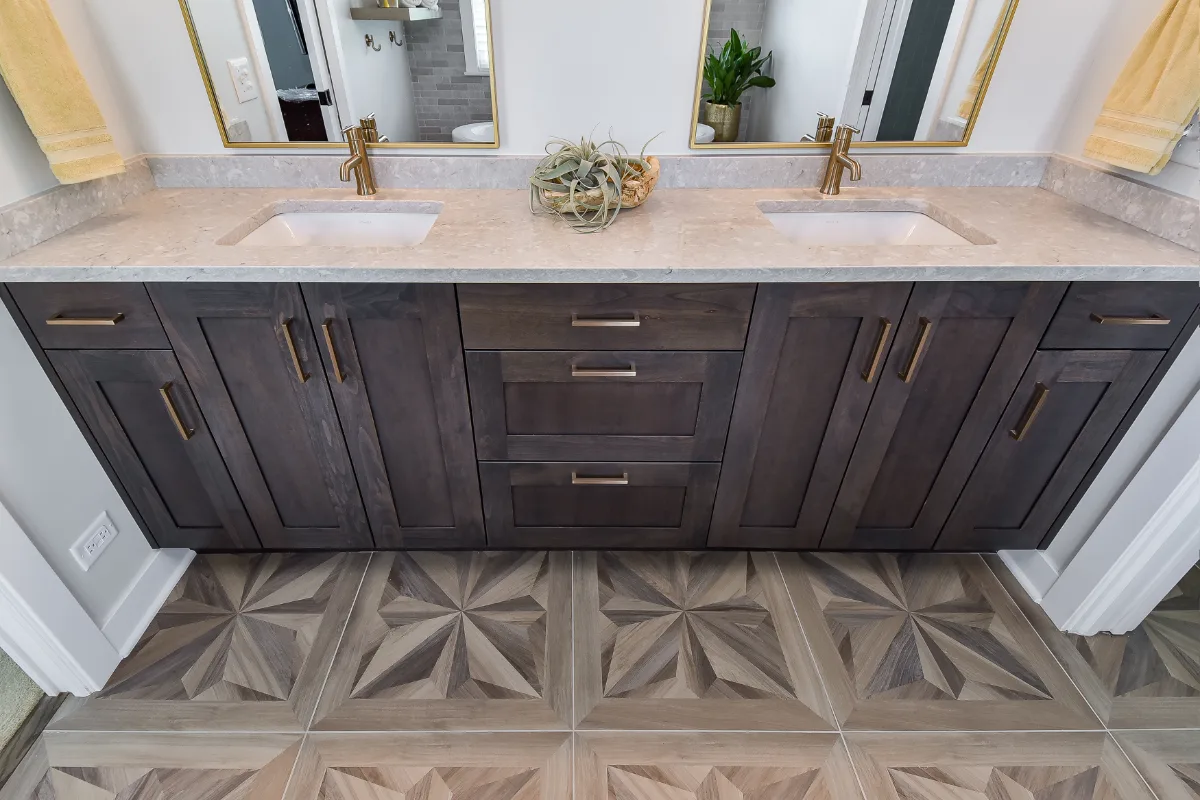 A rustic-warm primary bath in Franklin, TN. Bellmont Alder Folkstone cabinetry with Griege floating shelves, Orion Blanco Mist quartz, Delta Trinsic Champagne Bronze, Kohler Sunstruck tub, and Cassettone Honey Nut wood-look floor tile by Sebring.