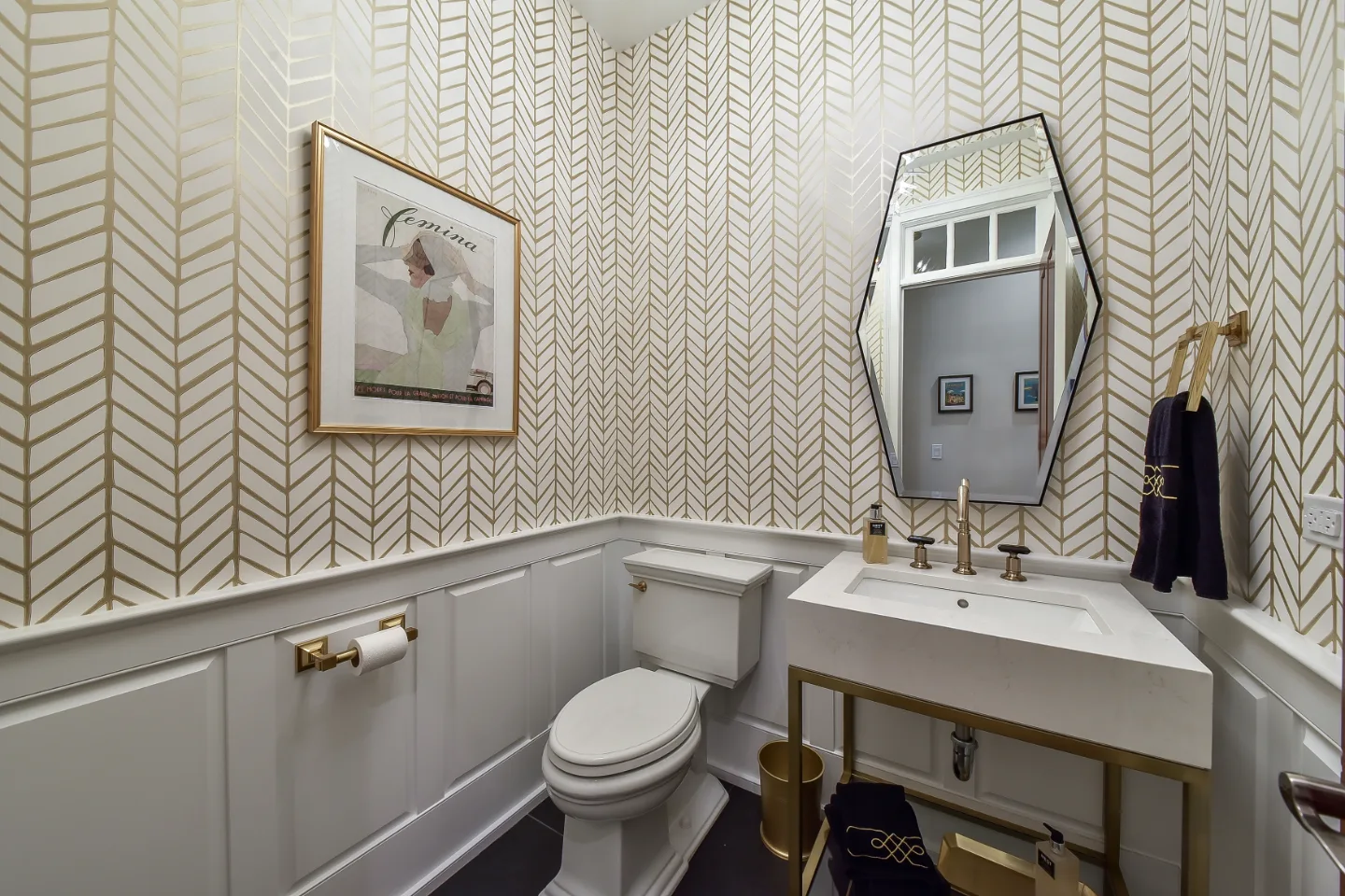 A transitional-elegant powder room in Brentwood, TN. RH Hudson Aged Brass vanity, CaesarStone Frosty Carrina quartz, Brizo Invari Luxe Gold faucet, and Serena and Lily Feather Gold wallpaper by Sebring Design Build.
