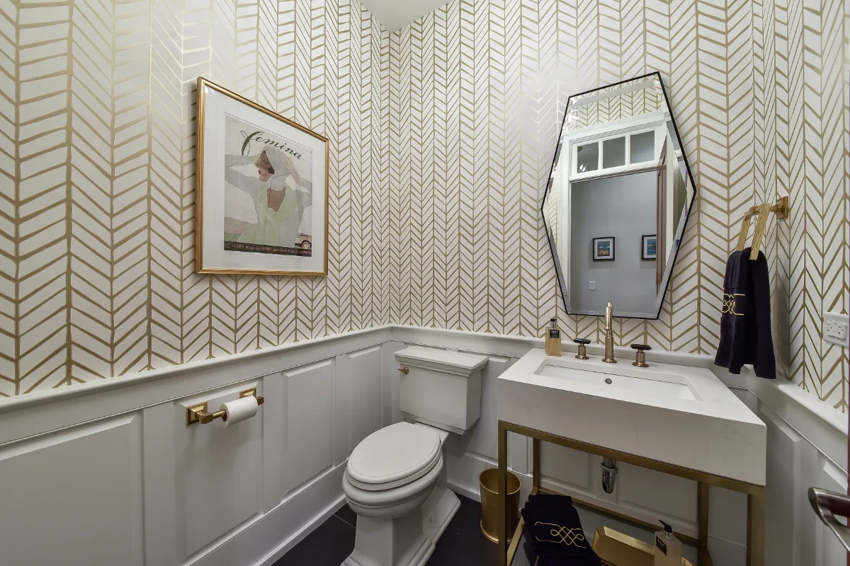 A transitional-elegant powder room in Brentwood, TN. RH Hudson Aged Brass vanity, CaesarStone Frosty Carrina quartz, Brizo Invari Luxe Gold faucet, and Serena and Lily Feather Gold wallpaper by Sebring Design Build.
