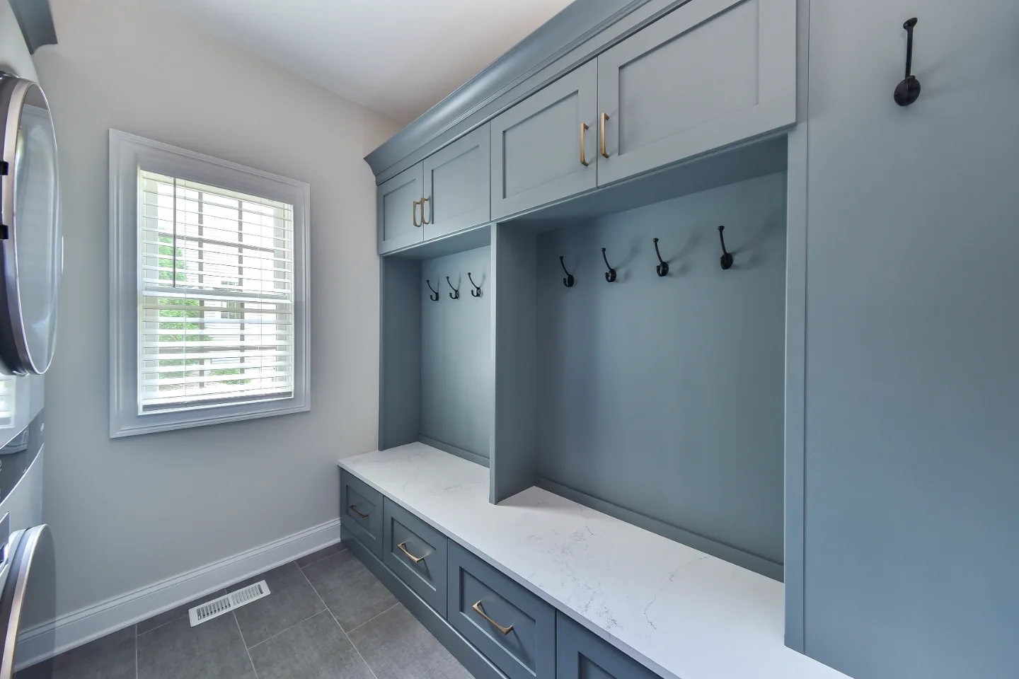 A transitional-functional mudroom in Brentwood, TN. Paint-grade Puget Sound cabinetry, CaesarStone Palm Shade honed quartz, Honey Bronze Top Knobs hardware, and Faroe Mother of Pearl flooring by Sebring Design Build.