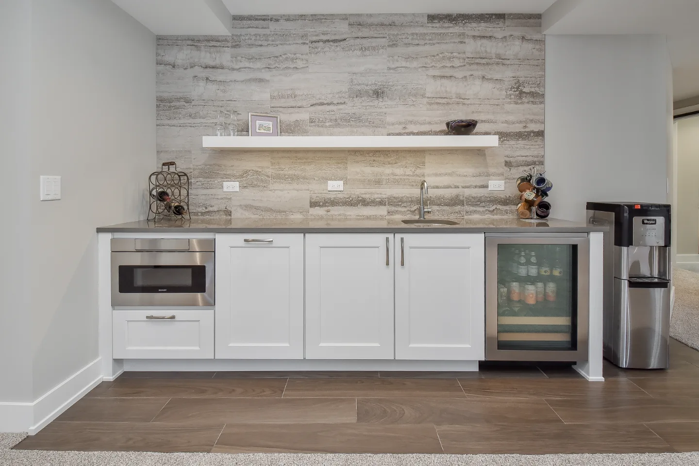 A functional-modern basement bar in Franklin, TN. Bishop Glacier White cabinetry, Cambria Devon quartz, Delta Trinsic Arctic Stainless sink, and Magnifica Silver backsplash by Sebring Design Build.