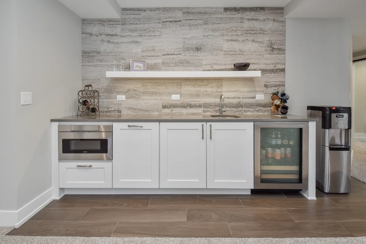 A functional-modern basement bar in Franklin, TN. Bishop Glacier White cabinetry, Cambria Devon quartz, Delta Trinsic Arctic Stainless sink, and Magnifica Silver backsplash by Sebring Design Build.