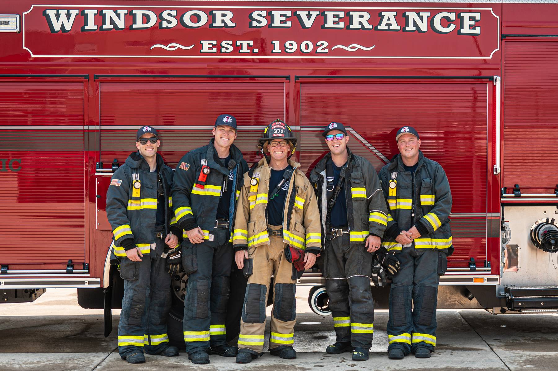 Five firefighters in uniform standing in front of a red fire truck with Windsor Severance lettering.
