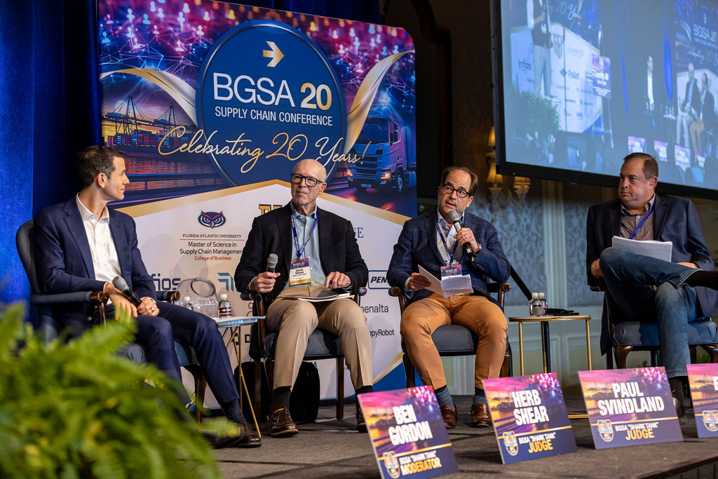 Four men seated on stage at BGSA 20 Supply Chain Conference with name tags and microphones.