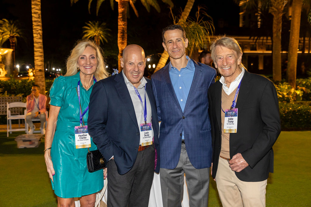 Four adults smiling and posing outdoors at night with palm trees and lights in the background.