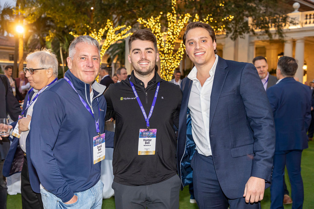 Four adults smiling at an outdoor nighttime event, wearing conference badges and business casual clothes.
