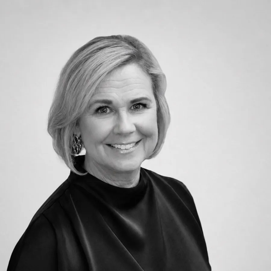 Porträtt på leende kvinna med kort ljus hår och mörk blus mot ljus bakgrund. LEKRI Sandviken Christina