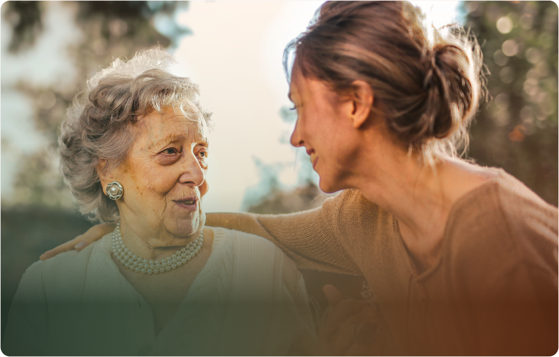 An older woman and a younger woman smiling at each other outdoors