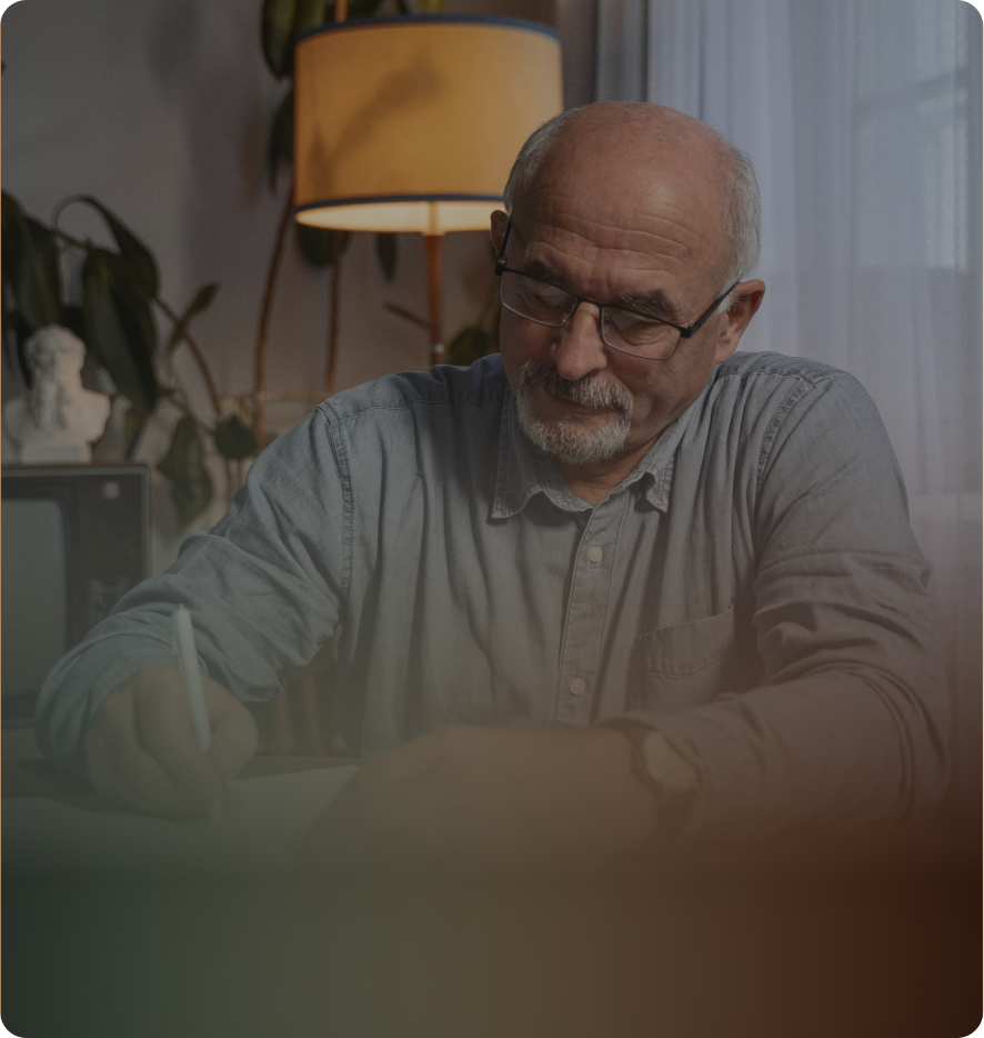 An older man writing at a desk at home