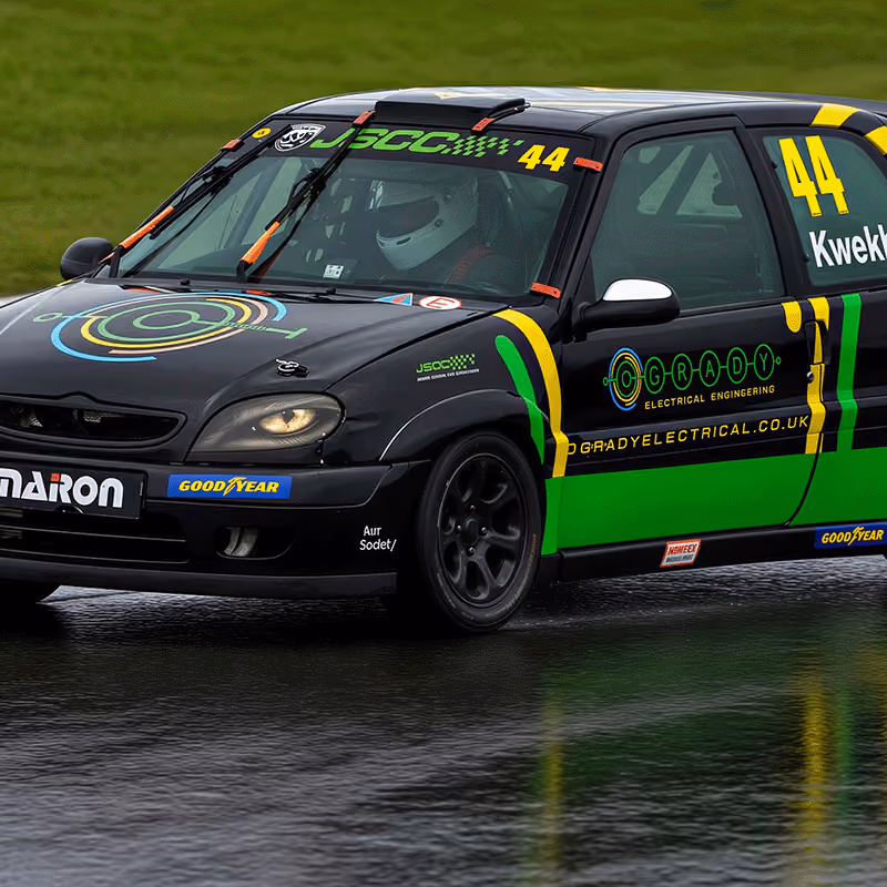 Black and green race car with number 44 and driver wearing a white helmet on a wet race track, featuring sponsorship logos including Goodyear and Grady Electrical Engineering.