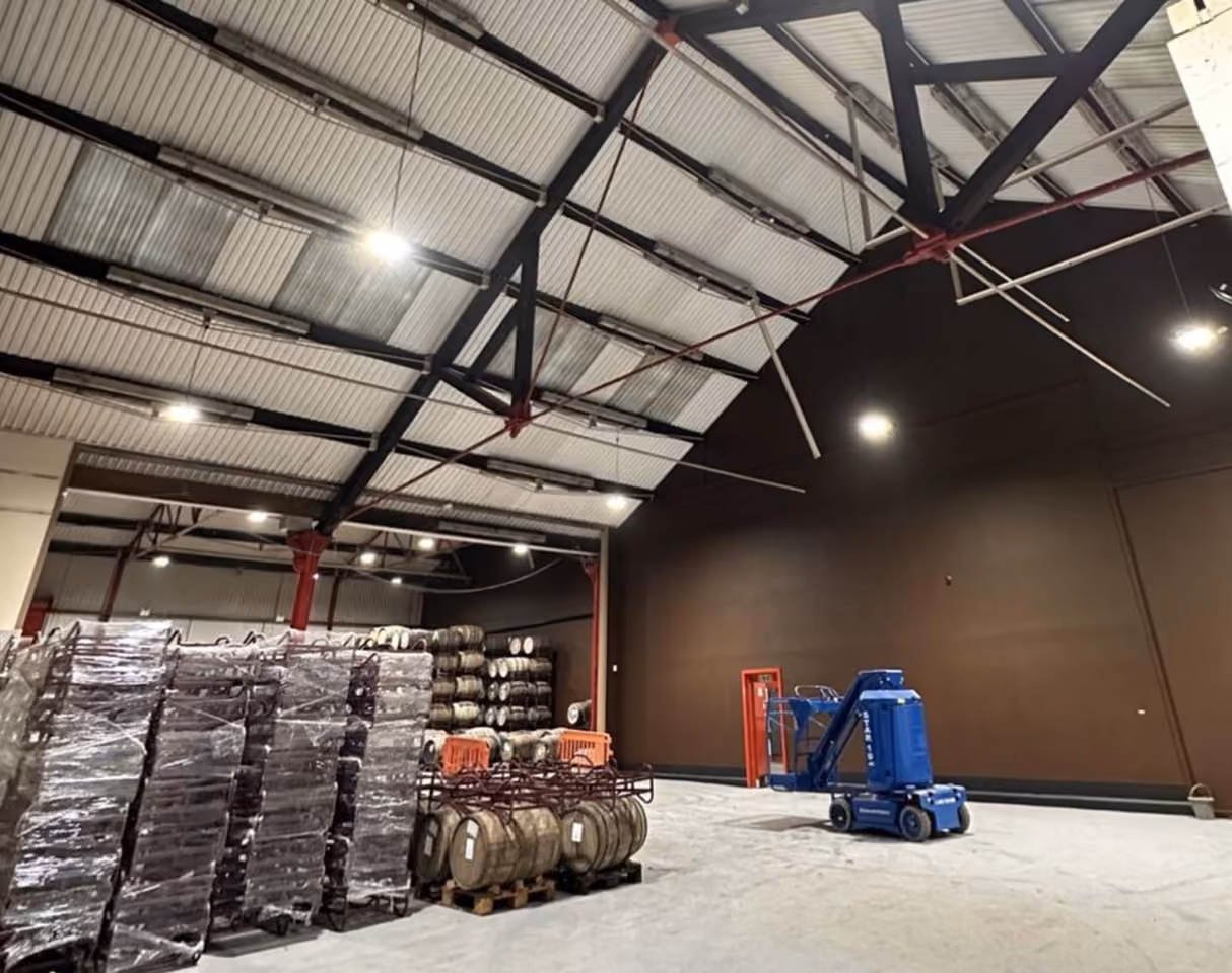 Inside a warehouse storing machinery with a high roof which has a number of large lighting units