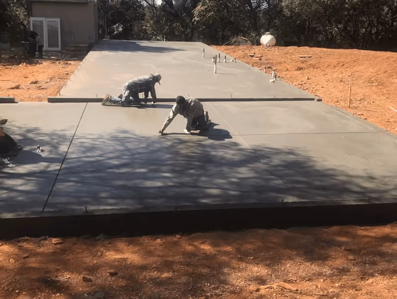 Three workers smoothing and finishing a newly poured concrete driveway on a sunny day.