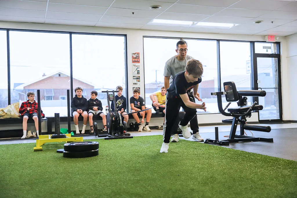 Coach observing a young athlete's swing technique during group training at Core Sport and Physical Therapy in Evergreen Park, IL.