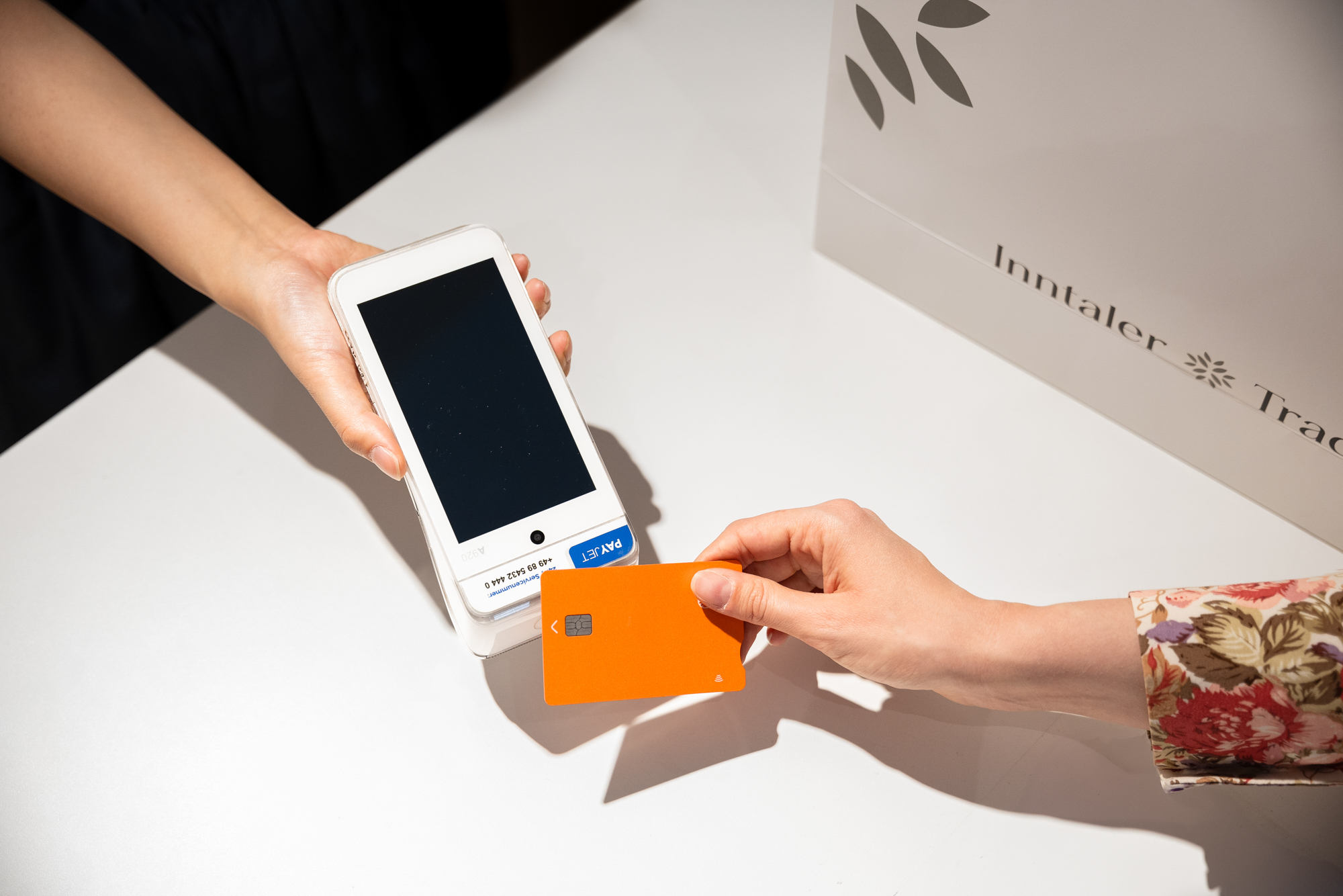 Kundin bezahlt kontaktlos mit orangefarbener Karte am mobilen Kartenterminal im Trachtengeschäft