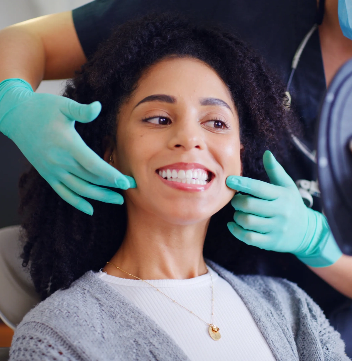 Close-up of bright white smile with turquoise-gloved hands framing mouth, shallow depth of field
