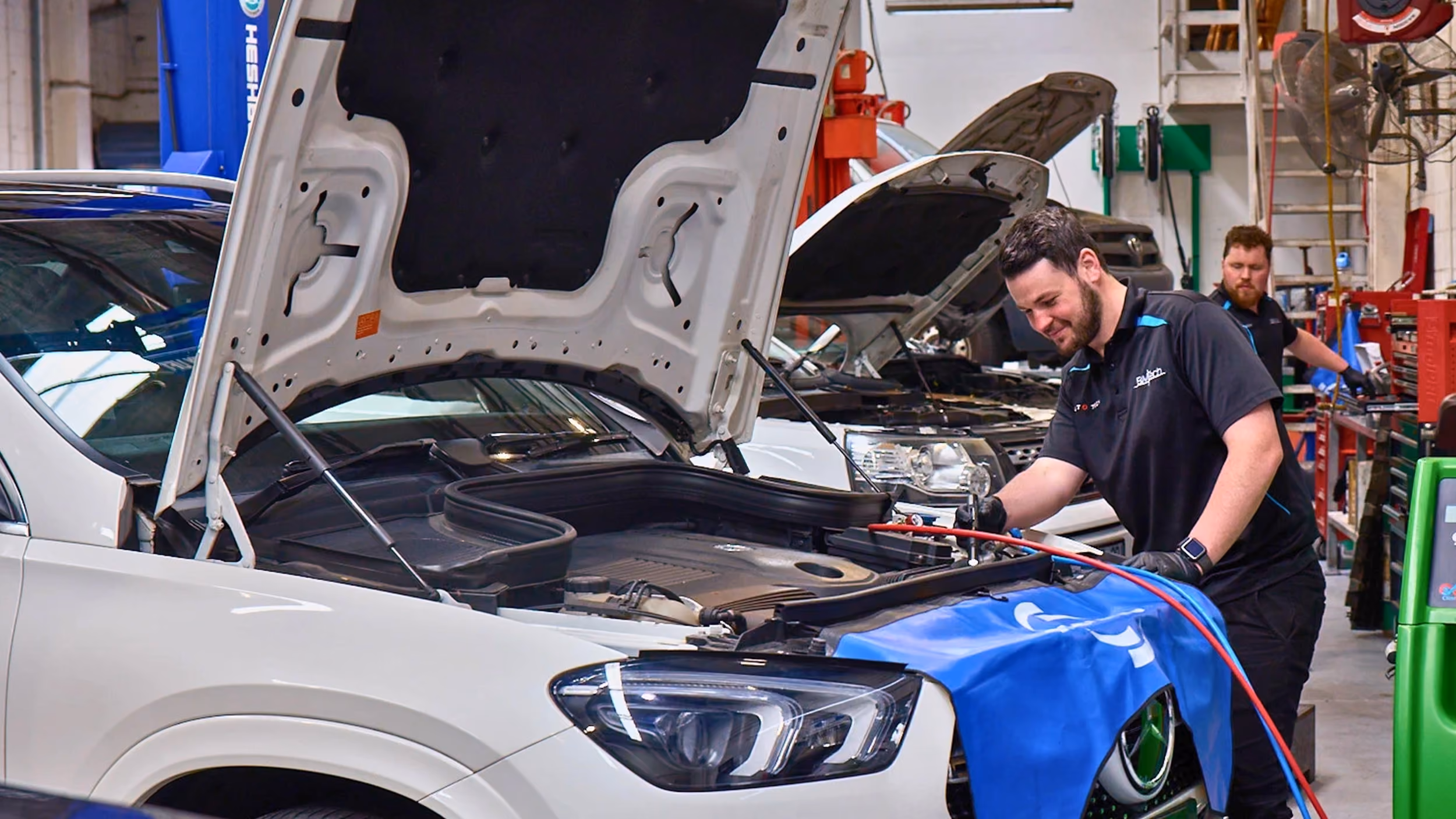 Automotive technician servicing a white vehicle with the bonnet open in a modern Auto Tech Group workshop.