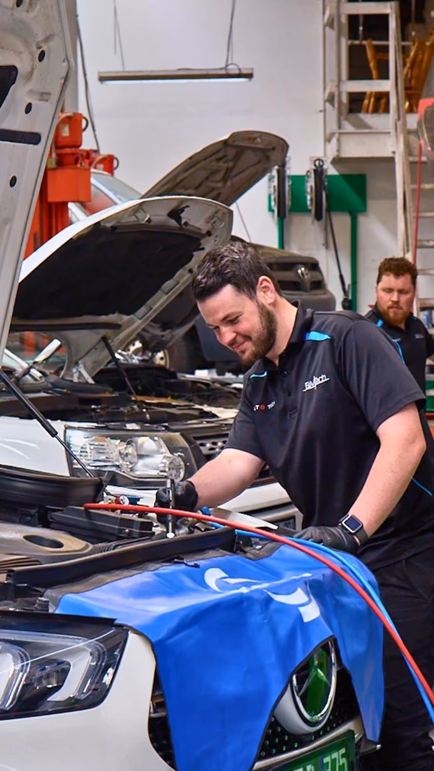 Automotive technician servicing a white vehicle with the bonnet open in a modern Auto Tech Group workshop.