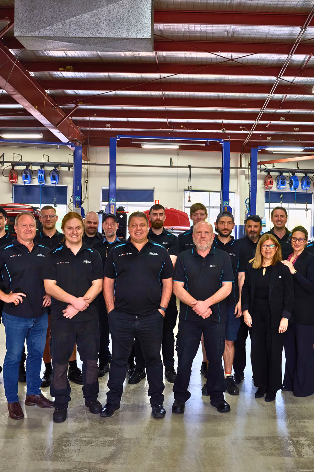 Group of mechanics and staff standing in an auto repair shop with cars and lifts in the background.
