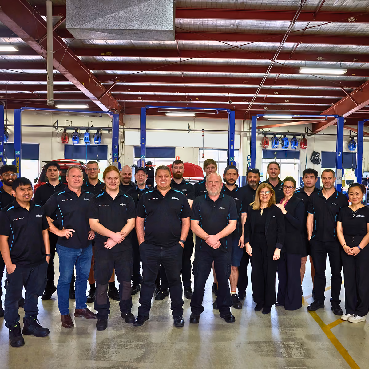 A group of 20 people posing inside an auto repair garage.