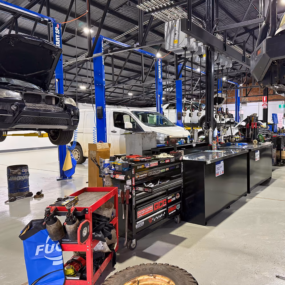 Interior of an auto repair shop with cars on lifts and tool cabinets on a clean concrete floor.