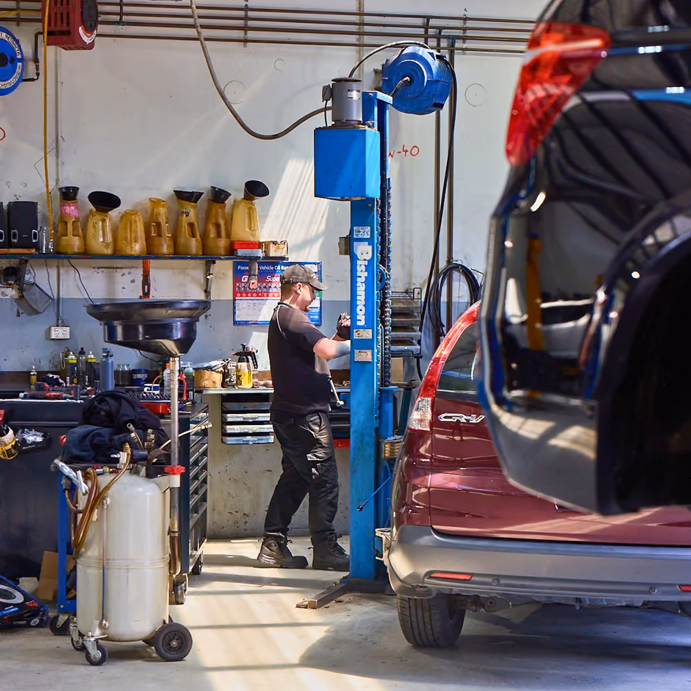 Technician working in workshop with tools and equipment beside vehicle.