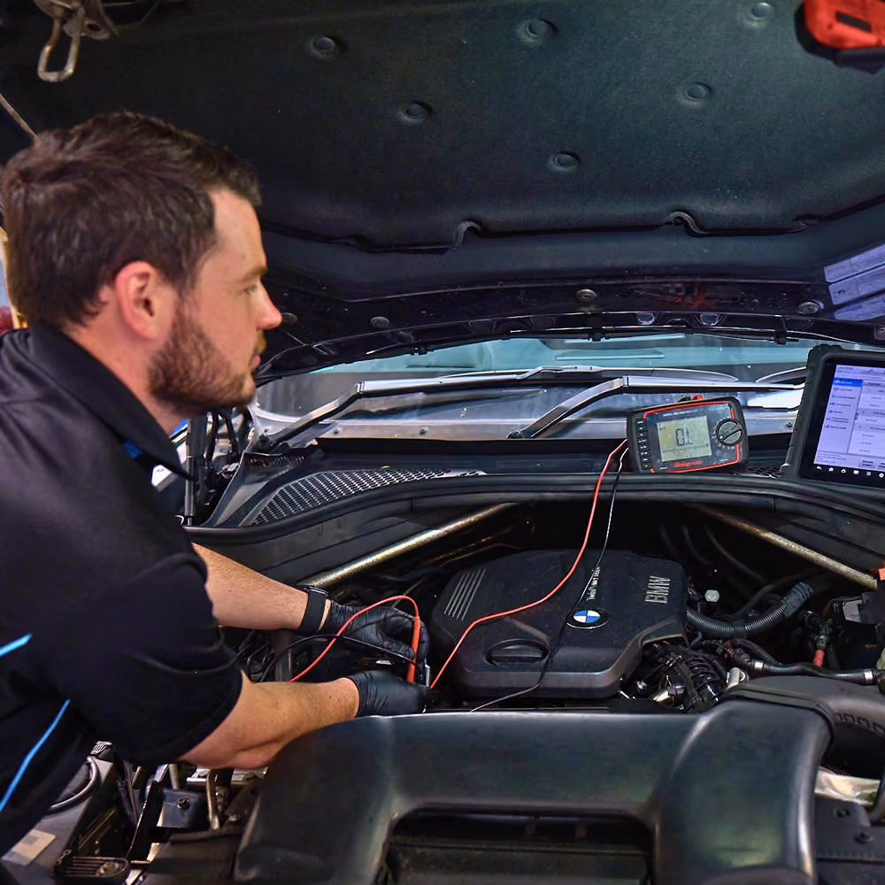 Technician running diagnostics on car engine during service.