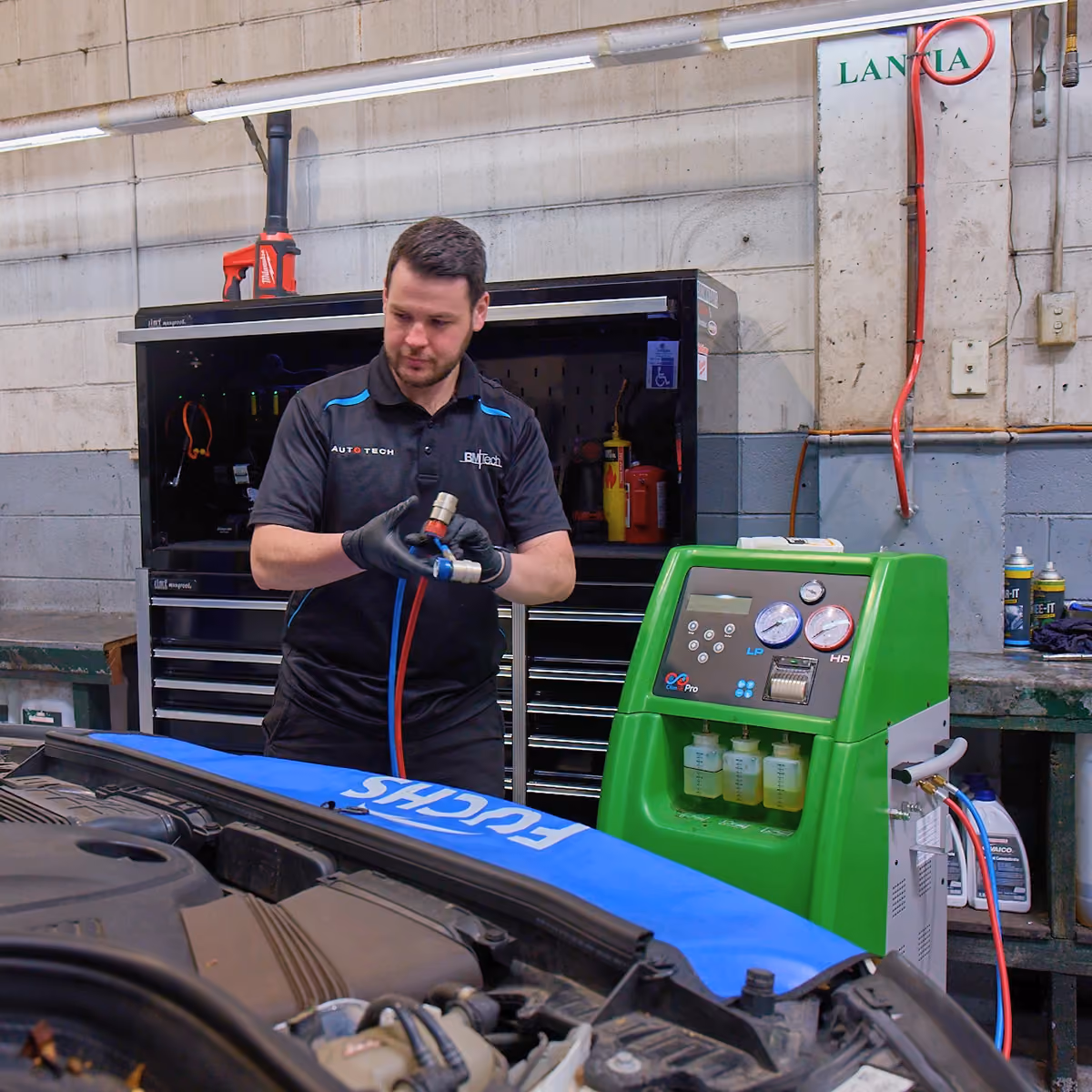 Auto technician servicing car air conditioning system and checking refrigerant levels.