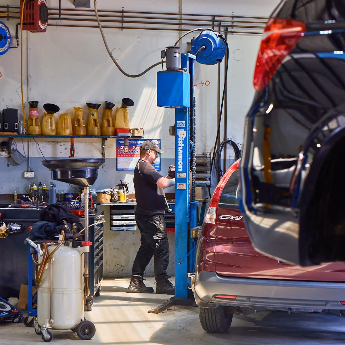 Technician carrying out repairs beside car in service bay.