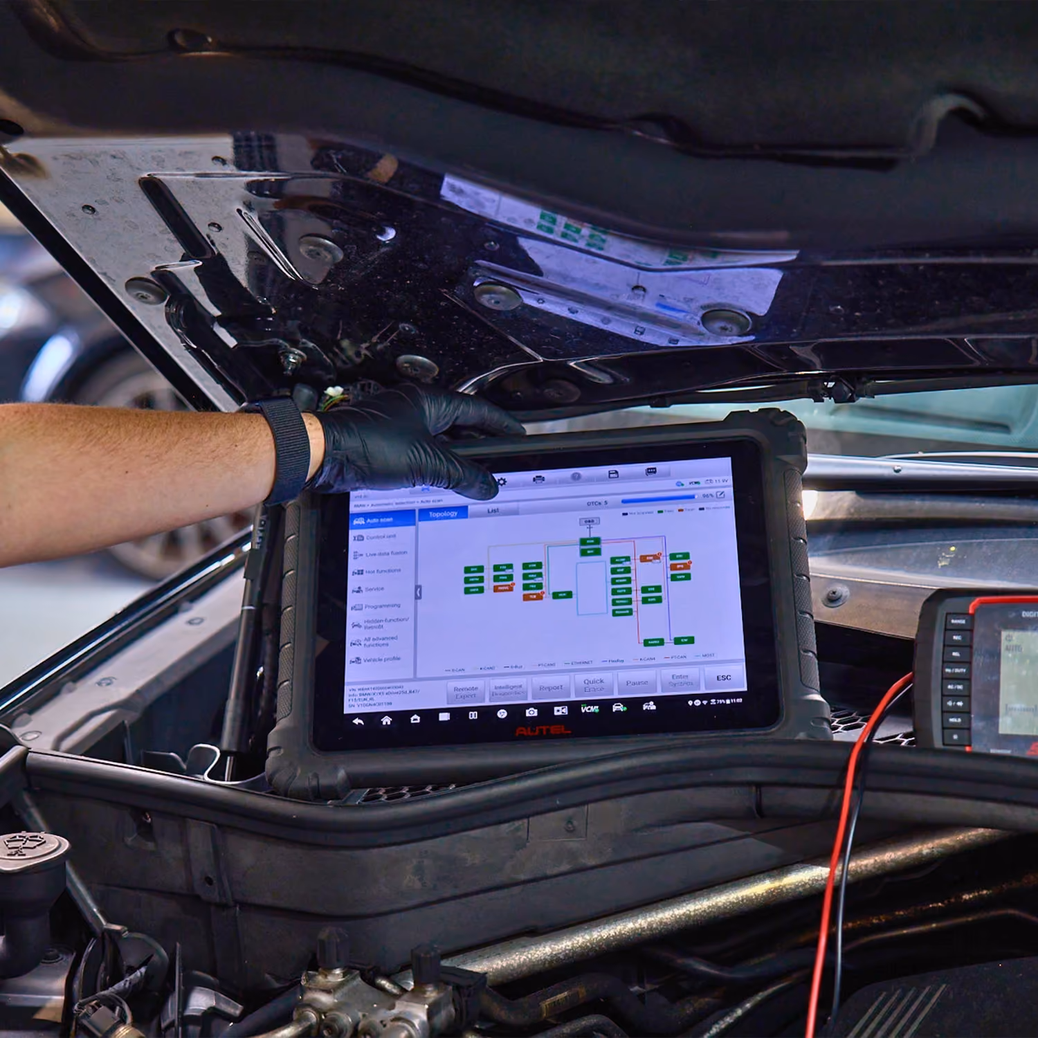 Technician using tablet diagnostic scanner to analyse car electrical system under bonnet.