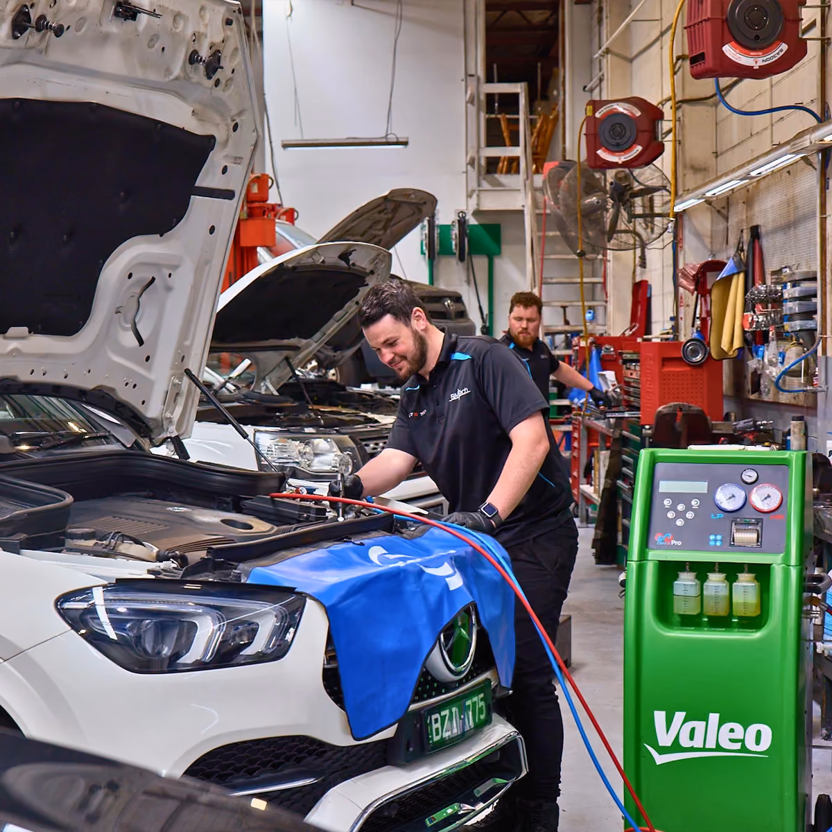 Mechanic repairing Mercedes engine with bonnet open.