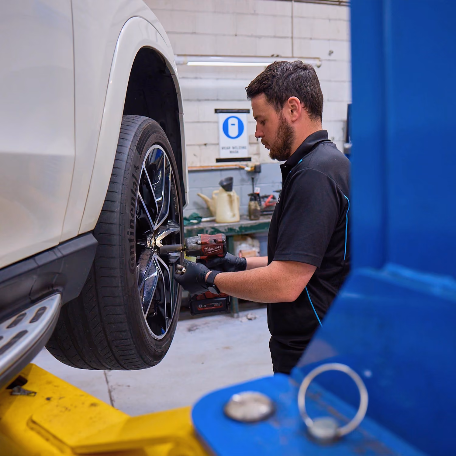 Mechanic tightening wheel on raised SUV in automotive workshop.