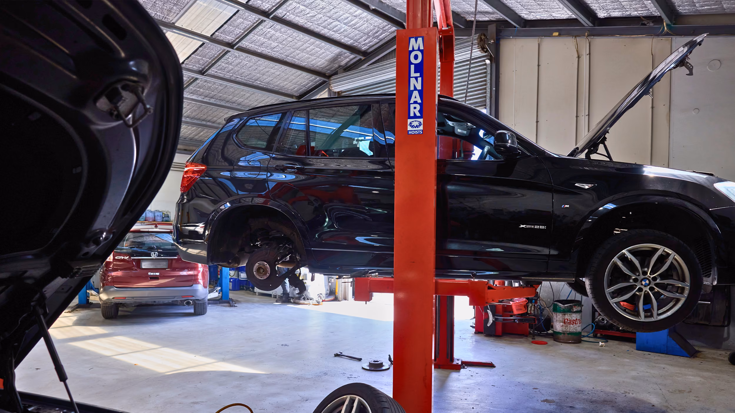 Car raised on hoist in workshop with wheel removed during mechanical inspection.