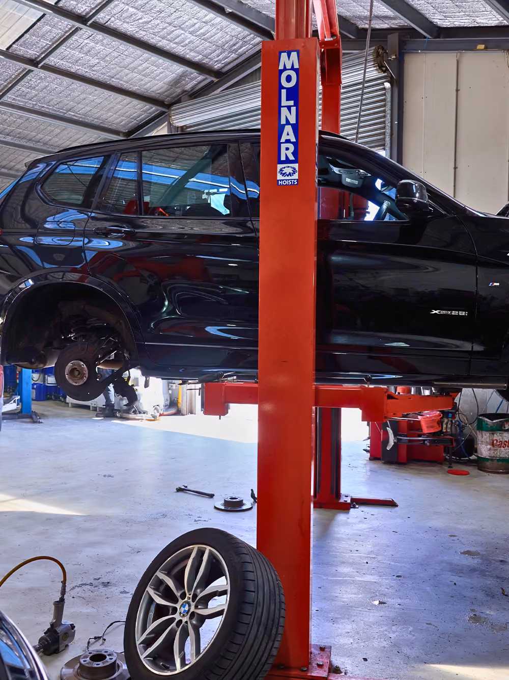 Car raised on hoist in workshop with wheel removed during mechanical inspection.