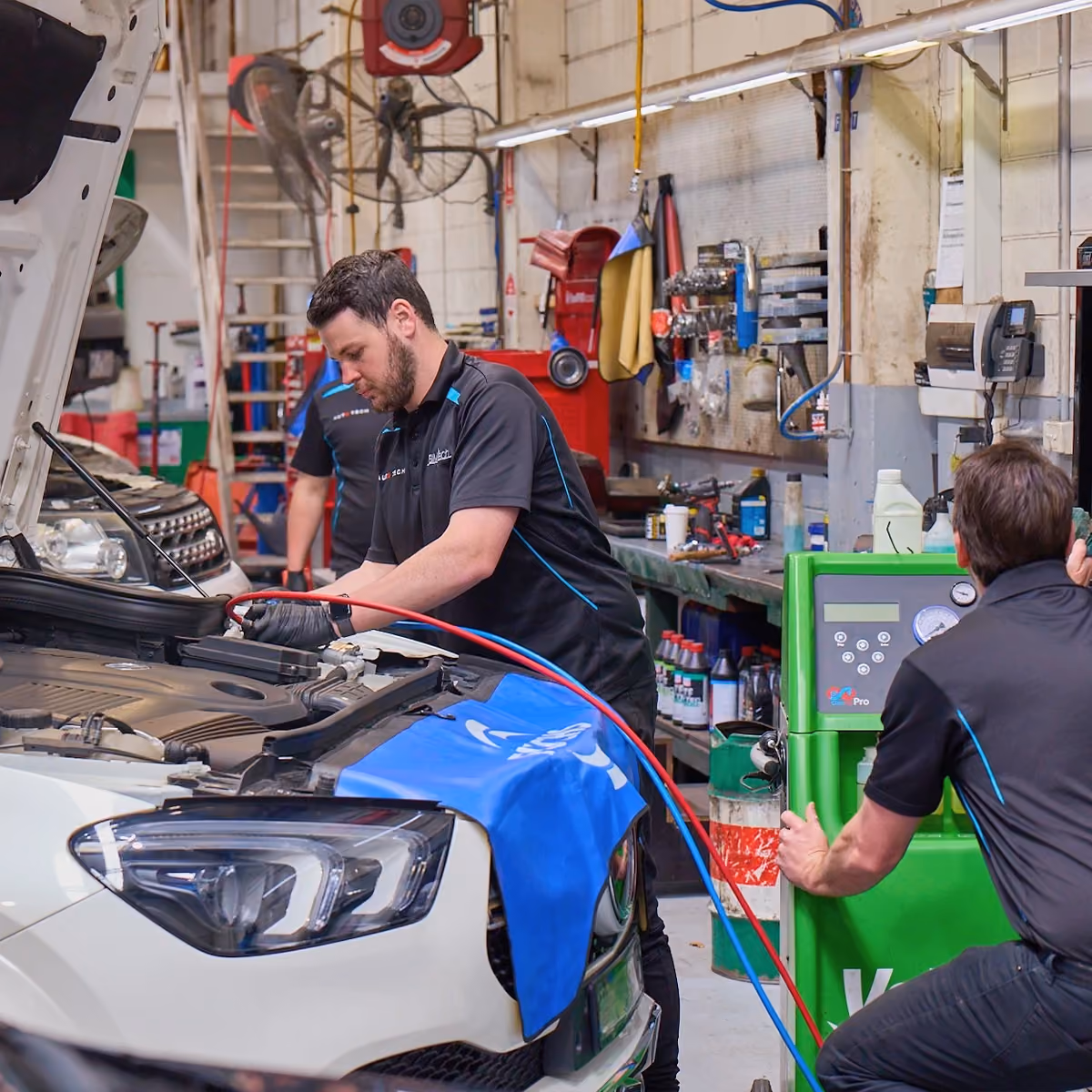 Technicians servicing a hybrid vehicle with diagnostic equipment in a busy workshop.